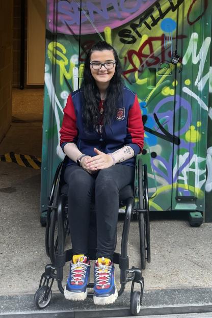 Young woman in wheelchair in front of graffitied wall.