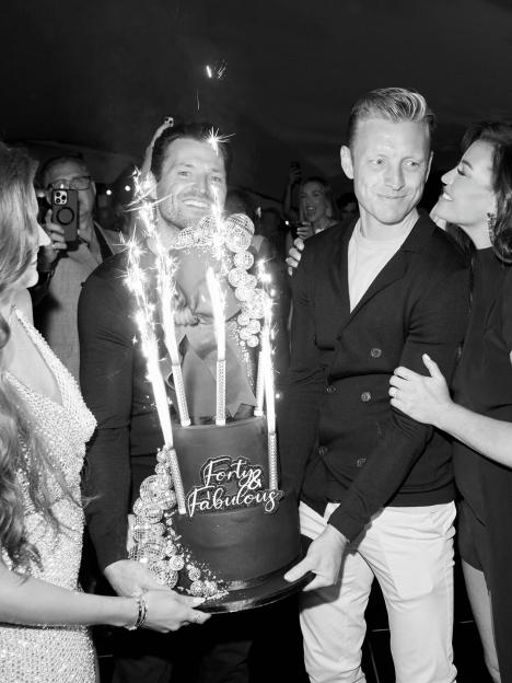 Black and white photo of a man smiling as he holds a "Forty & Fabulous" birthday cake with sparklers.