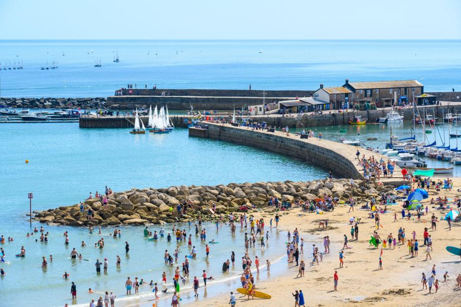 Crowded beach in Lyme Regis, Dorset with people swimming and relaxing.