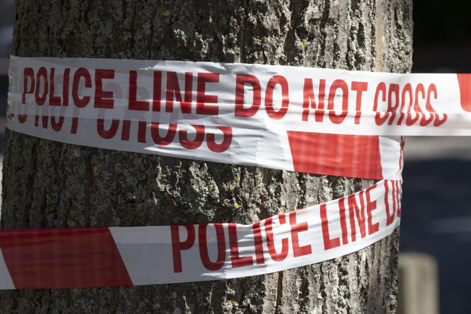 Police line do not cross tape wrapped around a tree trunk.