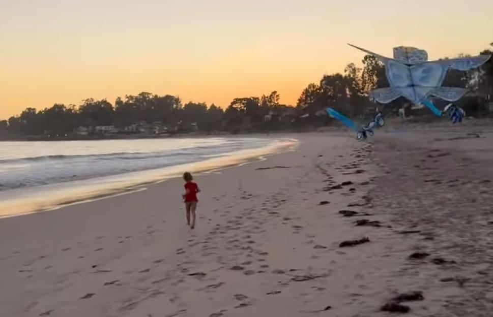 Girl running on beach at sunset with kites in the background.