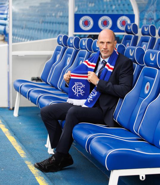 Philippe Clement, new Rangers manager, sits on a blue bench holding a blue and white Rangers scarf.