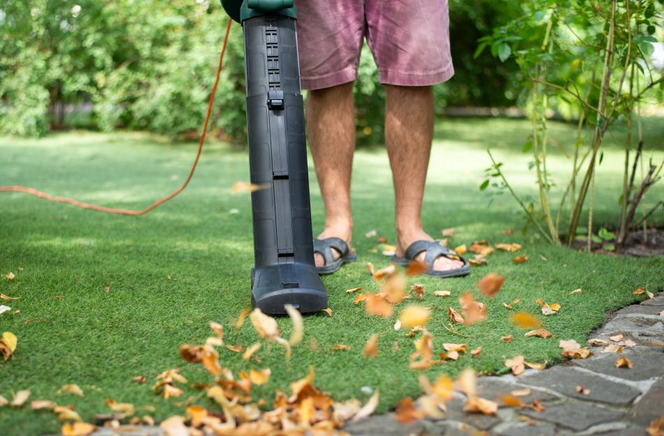 Person using a leaf blower to clean leaves from a lawn.