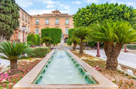 Fountain in a Spanish square with palm trees and flowers.