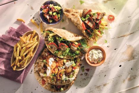 Overhead view of three gyros, french fries, and a Greek salad.