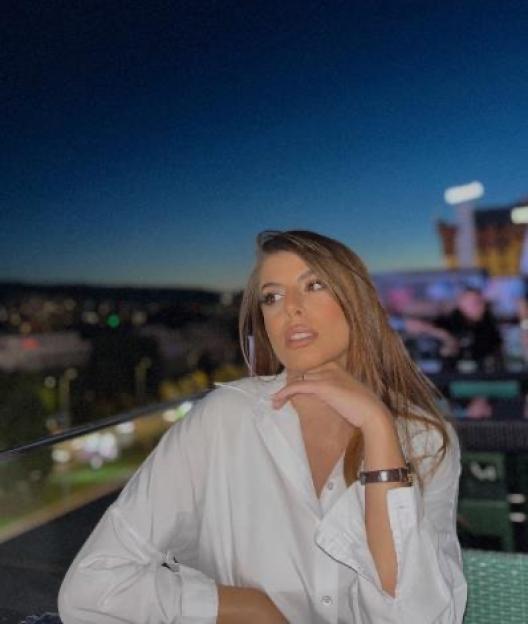 Adna Rovcanin-Omerbegovic wearing a white shirt with a dark city skyline in the background.
