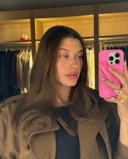 Hailey Bieber holding a pink phone and lip product.