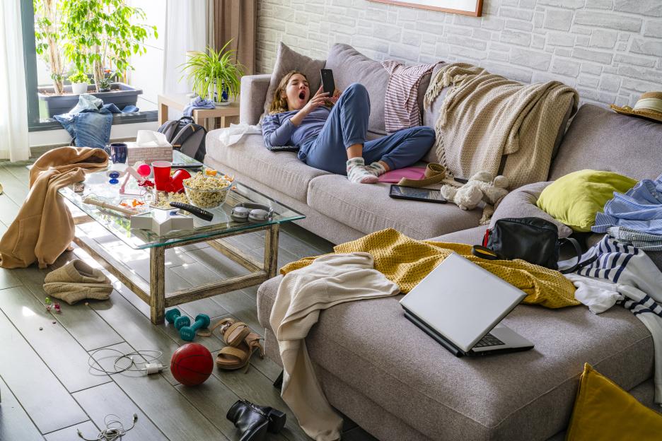 Young woman lounging on a couch in a messy living room.
