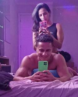 A man and woman taking selfies in bed.