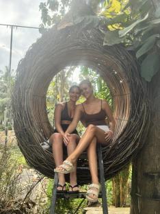 Two women sitting in a large woven nest-like structure.