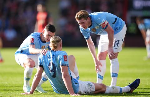 Erling Haaland on the ground with teammates attending to him.
