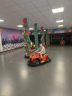 Boy driving a red kiddie ATV in an indoor race track.