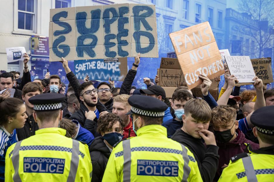 Chelsea Football Club fans protest against the European Super League, holding signs that say "SUPER GREED," "FANS NOT CUSTOMERS," and "SAVE THE BRIDGE."