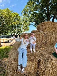 Woman and toddler sitting on hay bales, giving thumbs up.