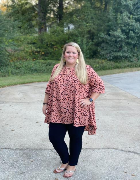 Woman wearing a pink and black patterned top and black leggings.