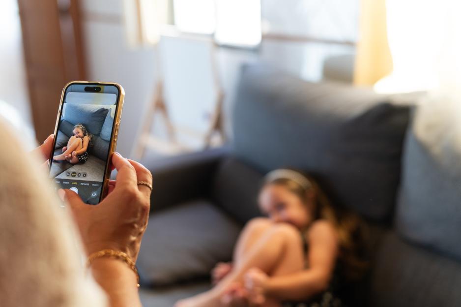 A mother taking a picture of her daughter on a sofa with a smartphone.