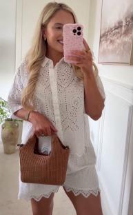 Woman modeling a white eyelet short set and brown handbag.