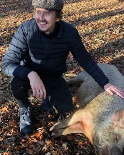 Matt King, known for his role as Super Hans in Peep Show, crouching next to a pig.