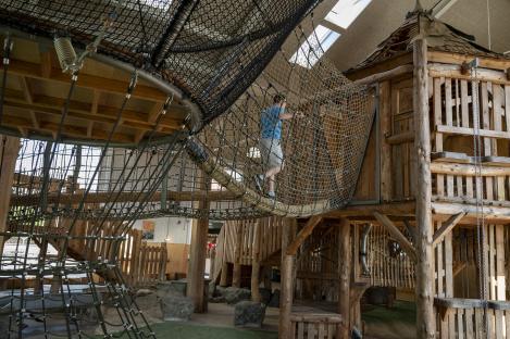 Person crossing a rope bridge on a wooden playground structure.