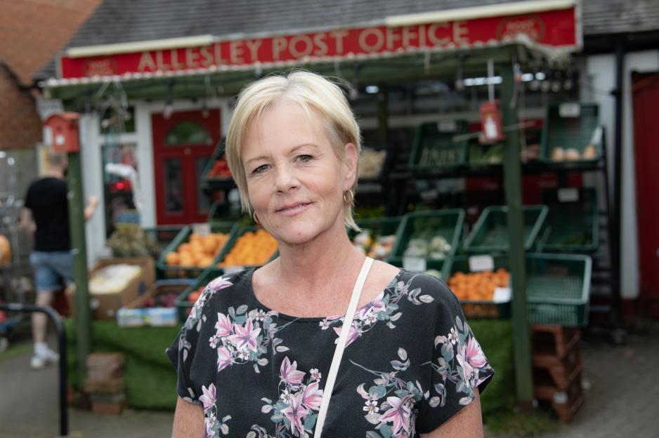 Photo of Jane Ascroft, a resident of Allesley, Coventry, standing in front of a post office and produce stand.