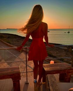 Woman in red dress watching sunset over ocean.