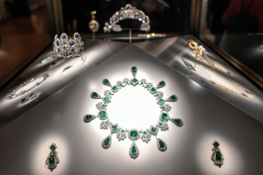 A dazzling emerald and diamond necklace with matching earrings displayed with other jewelry.