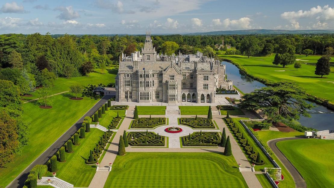 Adare Manor Golf Club, Limerick, with a large stone building and manicured gardens next to a river and golf course.