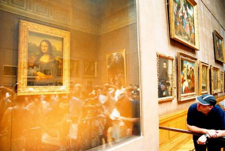 A man views the Mona Lisa through a protective glass case in a museum.
