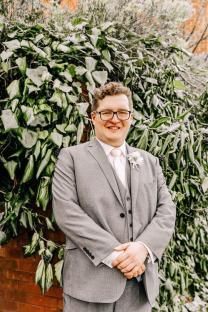 Man in gray suit standing in front of a green wall.
