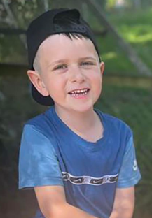 Smiling young boy wearing a blue shirt and black baseball cap.