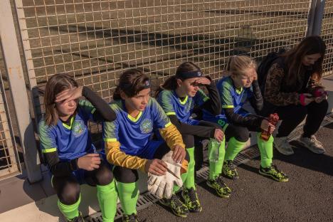 Girls' soccer team from Kherson, Ukraine, sitting near a fence before a match.