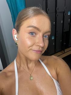 Woman wearing earbuds and necklace in front of lockers.