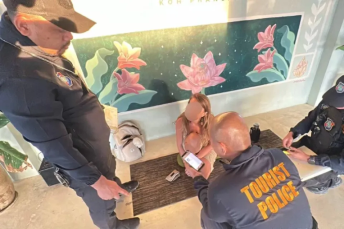 Three tourist police officers interviewing a woman on the floor holding a baby.