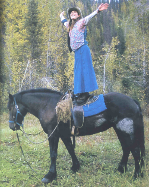 Woman standing on a horse with arms outstretched.