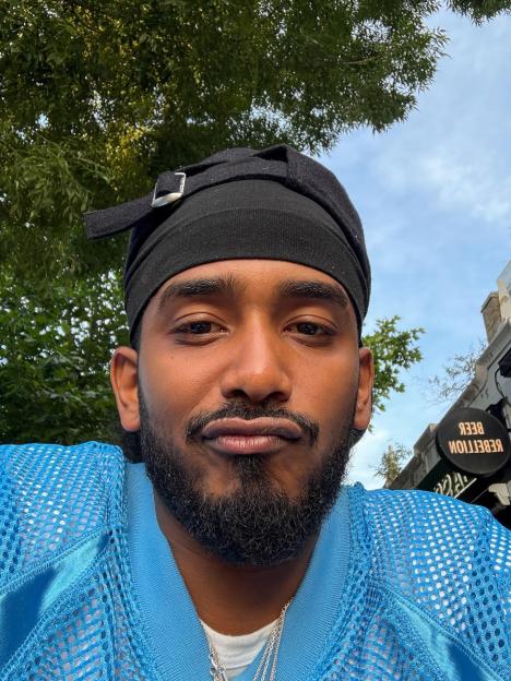 Close-up selfie of a man wearing a black cap and a light blue jersey.