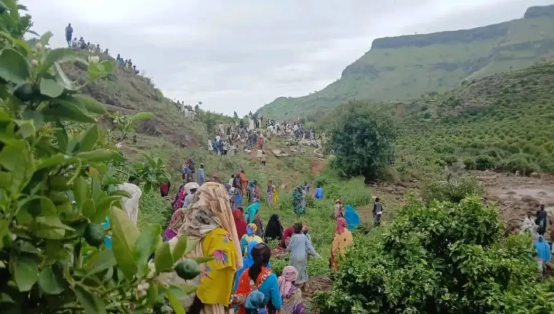 Large group of people gathered in a hilly area, possibly responding to a disaster.