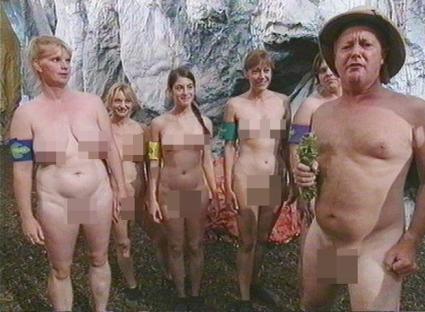 Group of nude adults standing in front of a rock wall.