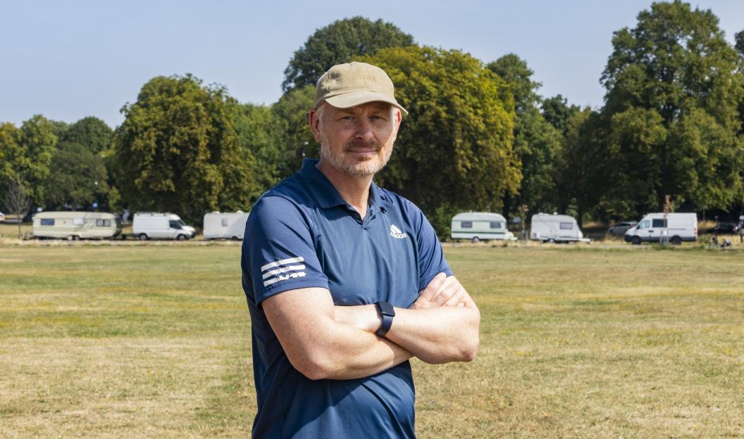 Tony Nelson, chair of the Protect the Downs group, stands with arms crossed. Vehicles are visible in the background.