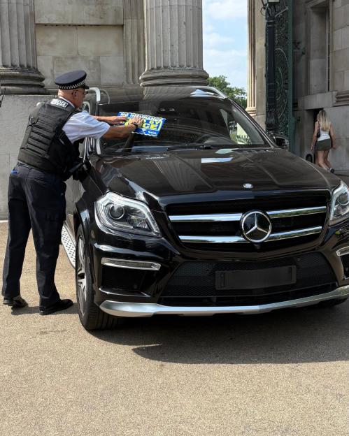 Police officer placing a "no insurance" notice on a Mercedes-Benz.