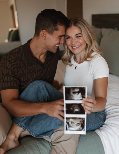A smiling couple sitting on a bed holding up ultrasound images.