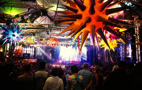 Large crowd at an indoor music festival with colorful decorations hanging from the ceiling.