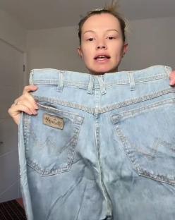 Woman holding up a pair of light wash jeans.