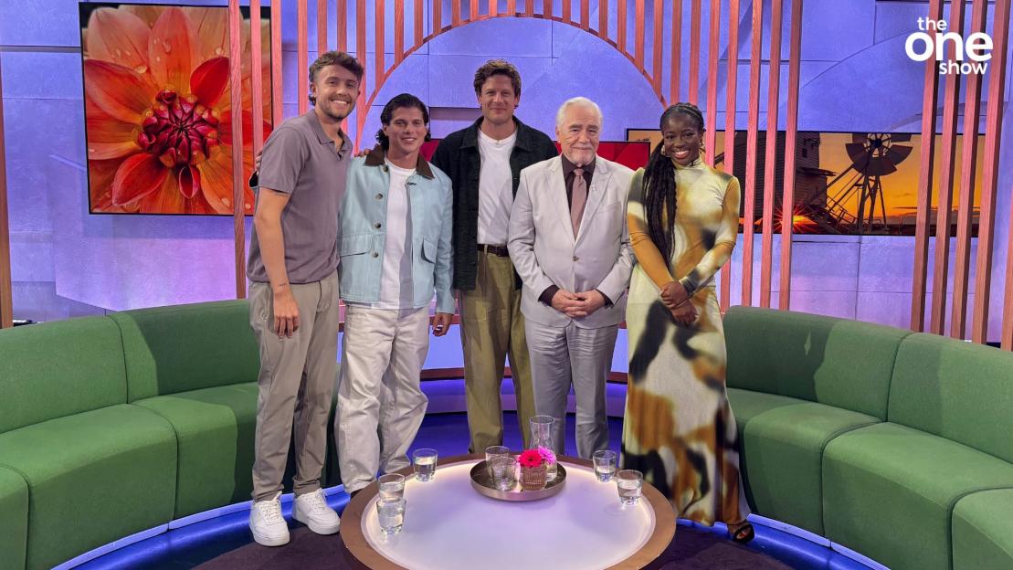 Five people posing on a talk show set.