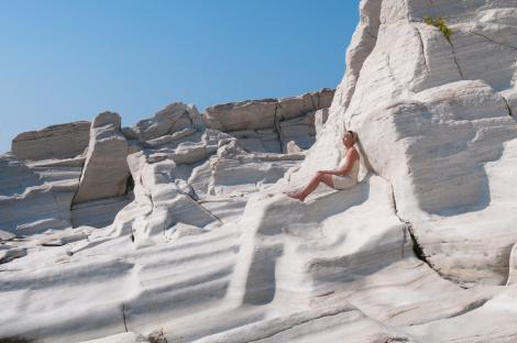 Woman sitting on white marble rocks in Thassos, Greece.