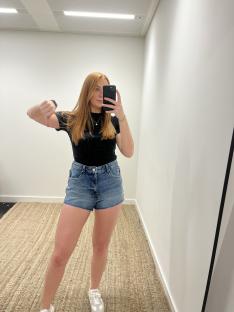 Woman giving a thumbs down while wearing denim shorts.