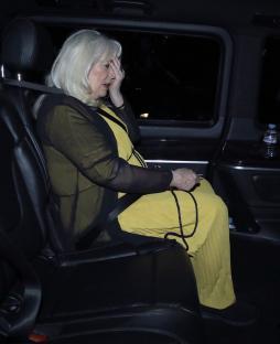 Woman in yellow dress sits in car, hand to face.