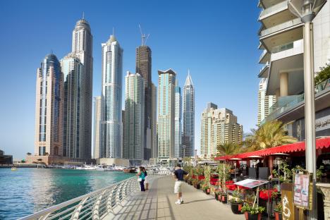 Dubai Marina waterfront with skyscrapers and people walking along a promenade with restaurants.