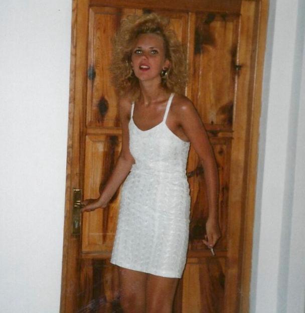 Photo of a woman in a white dress standing by a wooden door.
