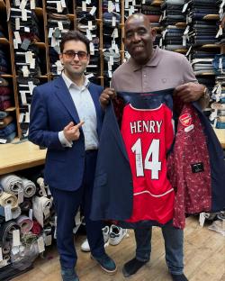 Man holding up a suit jacket with a Thierry Henry Arsenal jersey inside.