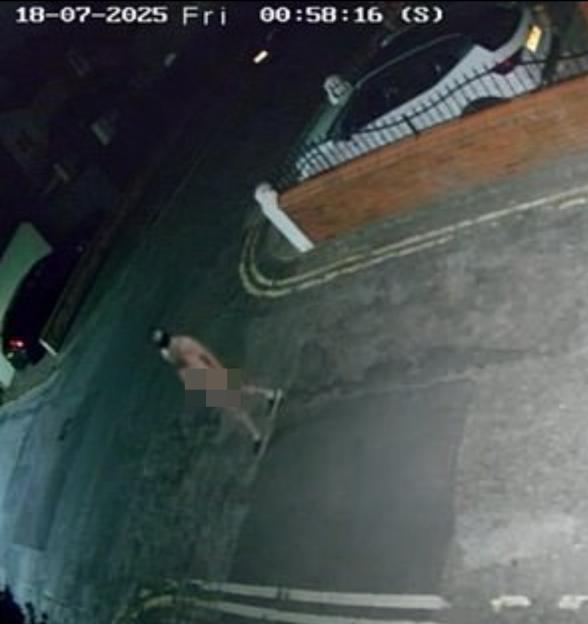 Security camera footage of a nude man walking down a street at night.